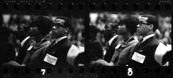 Black and white image of a negative, showing two different shots of the same couple, seated in a crowd.